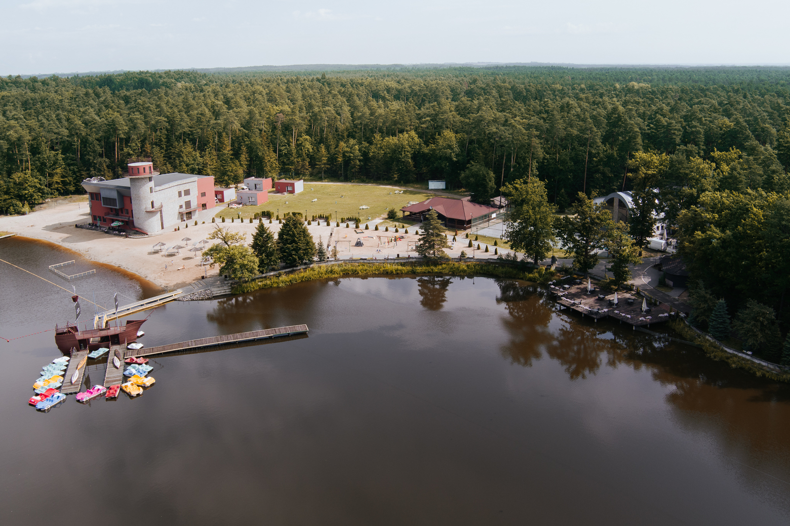 Widok z lotu ptaka na jezioro, plażę i kompleks rekreacyjny Grand Chotowa otoczony lasem